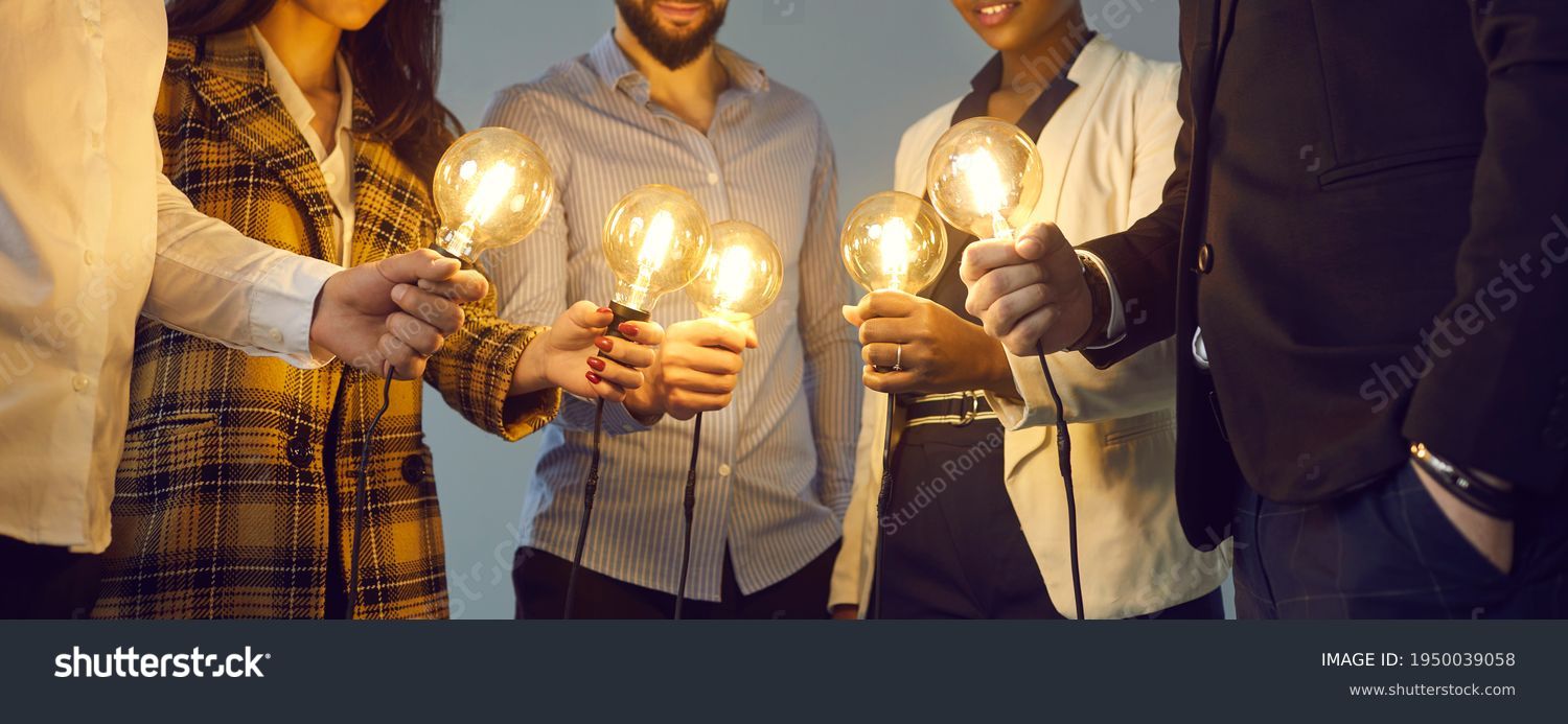 Background with young multiethnic business team holding glowing vintage Edison lightbulbs. Multiracial men and women join shining electric light bulbs as metaphor for teamwork and sharing creative #1950039058