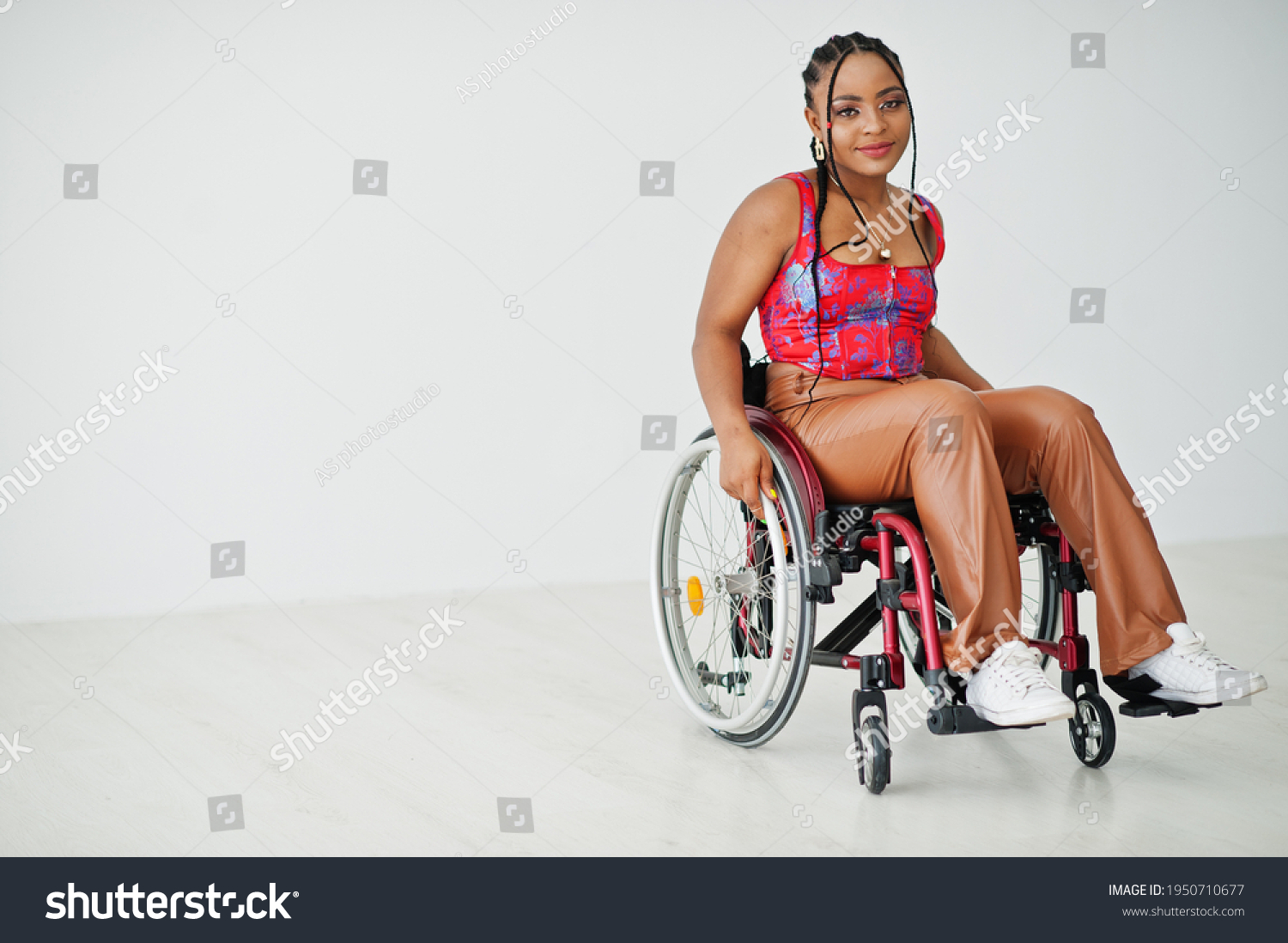 Young disabled African American woman in wheelchair against white wall. #1950710677
