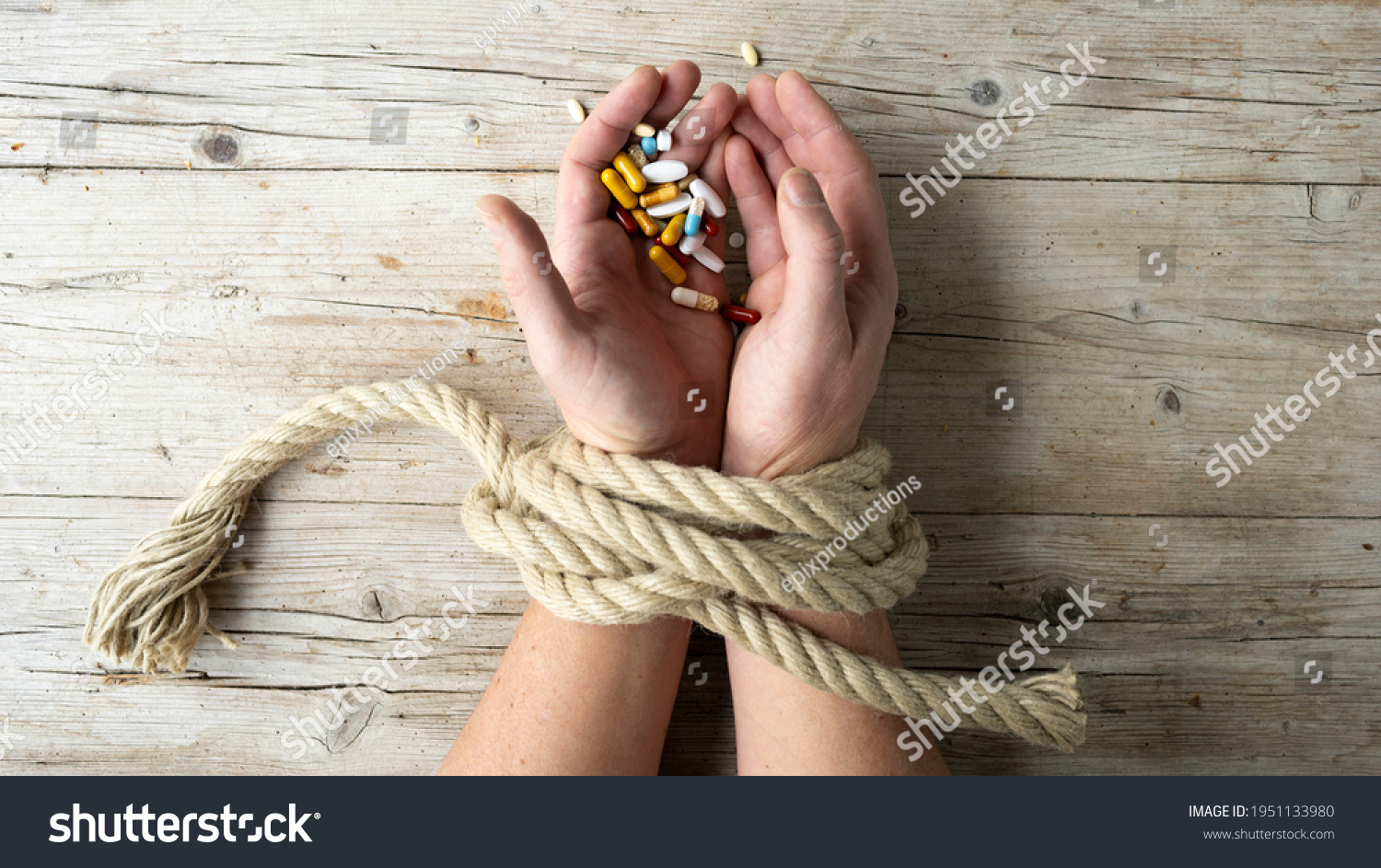 Hands of man are tied with a rope and in his hands he holds many different pills, concept addiction, drug addiction, photo taken from above #1951133980