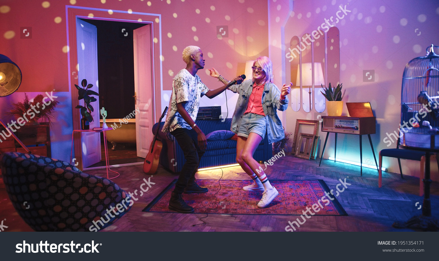 Two happy positive multi-ethnic youth dancing moving rhythmically in good mood at home party, male and female friends having fun energetically moving in room in neon disco light, retro style concept #1951354171