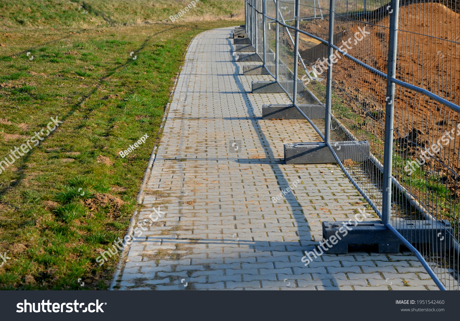 Construction sites with portable fence parts that are installed in plastic weight racks hold the stability of the fencing. along the sidewalk made of interlocking paving #1951542460