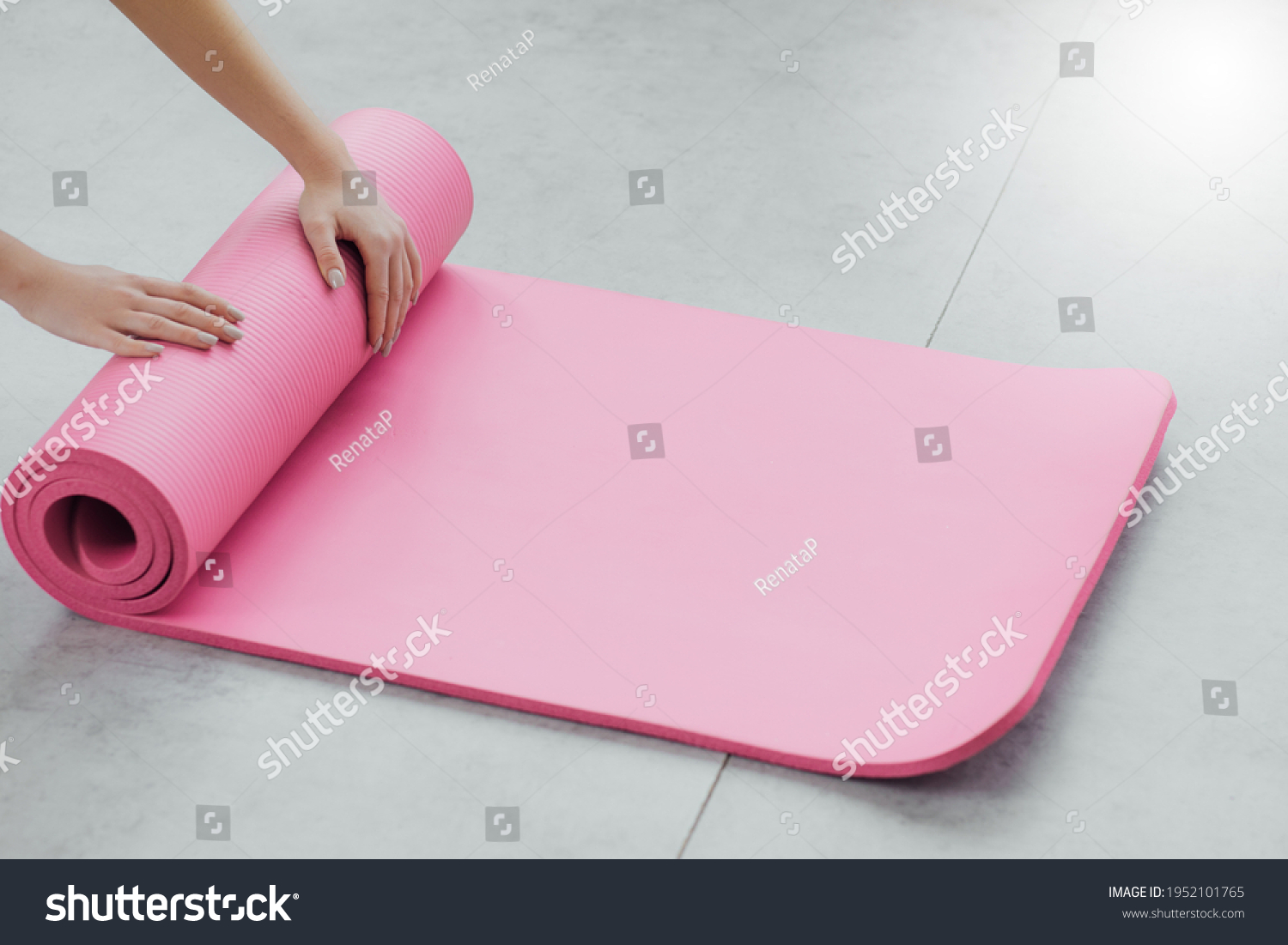 Time for meditation, fitness session, well-being concept. Girl wearing grey sporty pants rolling fitness mat before, after class in yoga studio club or at home on wooden floor. Hands and legs close up #1952101765