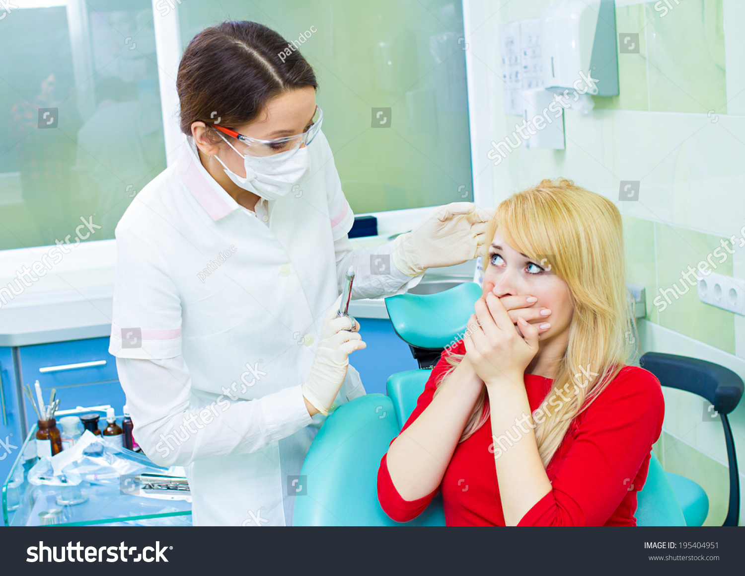 Closeup portrait young terrified girl woman scared at dentist visit, siting in chair, covering her mouth, doesn't want dental procedure, drilling, tooth extraction, isolated clinic office background #195404951