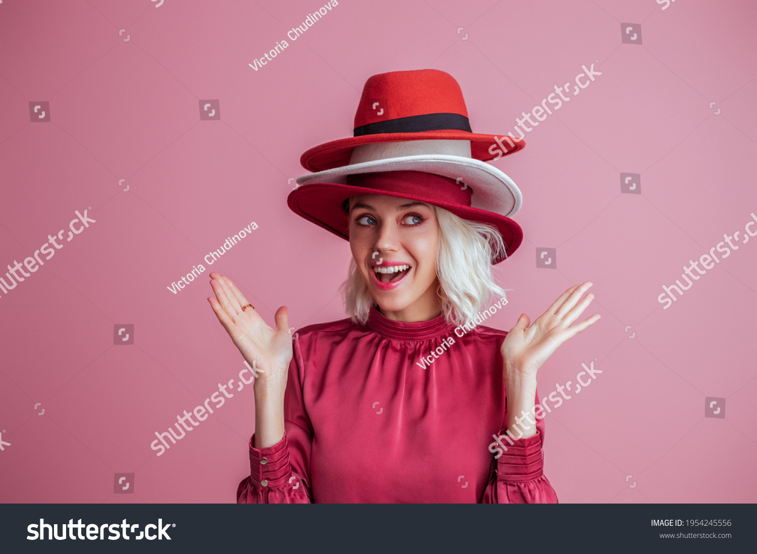 Funny fashionable woman wearing three hats, posing on pink background. Model looking up. Fashion, sale, shopping advertising conception. Copy, empty space for text #1954245556