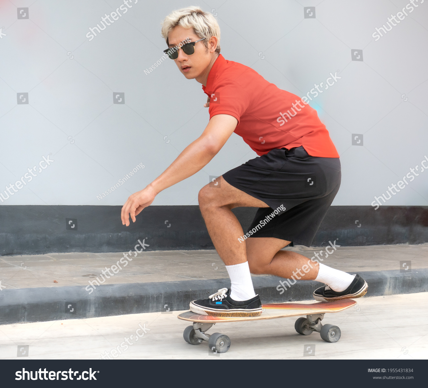 Young asian man riding skateboard on a city street. Portrait of male in t-shirt and black short pants exercise surf skate near sidewalk in urban. Trendy outdoor extreme sport recreation in Asia.  #1955431834