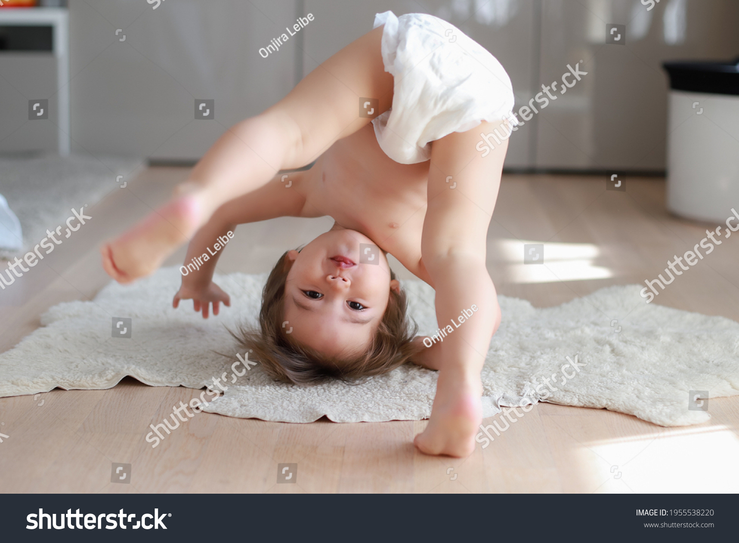Cute and funny baby boy wearing diaper bending over doing yoga or playing hide and seek at home. Happy mixed race Asian-German child play and learn development. #1955538220