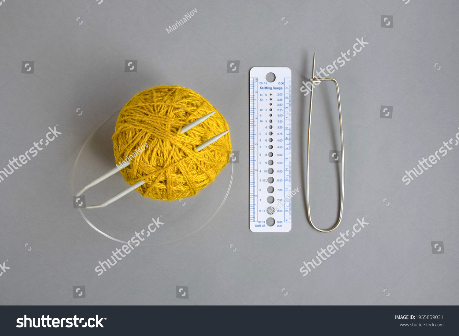 One skein of yellow wool yarn, knitting spokes, measuring ruler and large pin on gray background, handmade, knitting. Close-up. Copy space. Selective focus. #1955859031