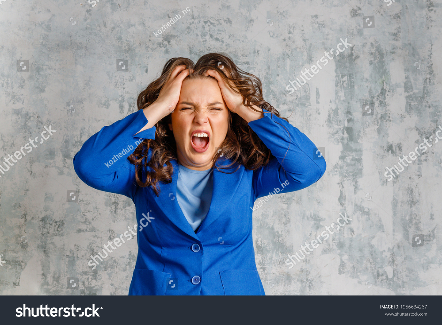 Furious  woman screaming and holding her head. Emotional  lady shouting in anger, being aggressive or mad, suffering from stress. headache. The young woman is angry and screaming, holding her head. #1956634267