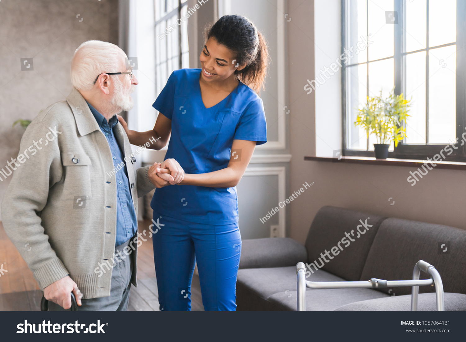 Young caring african nurse helping senior old elderly man grandfather walk . Disable old man trying to walk with the assistance aid of female doctor. #1957064131
