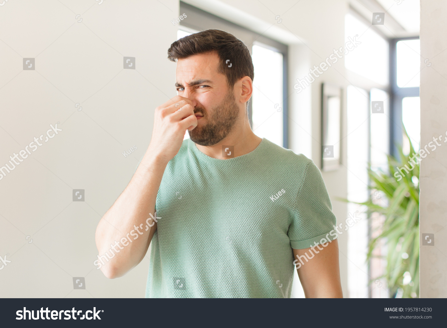 handsome man feeling disgusted, holding nose to avoid smelling a foul and unpleasant stench #1957814230