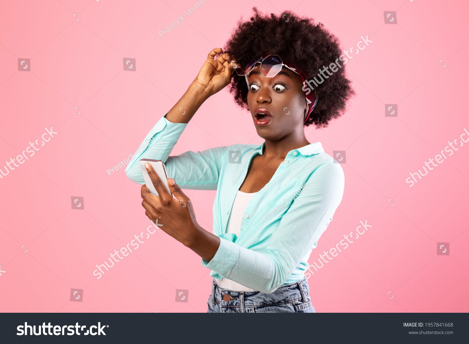 Wow Application. Extremely Shocked African Woman Looking At Smartphone Reading Message With Exciting Shocking News Holding Eyeglasses Posing Over Pink Studio Background. New Mobile App For Phone #1957841668
