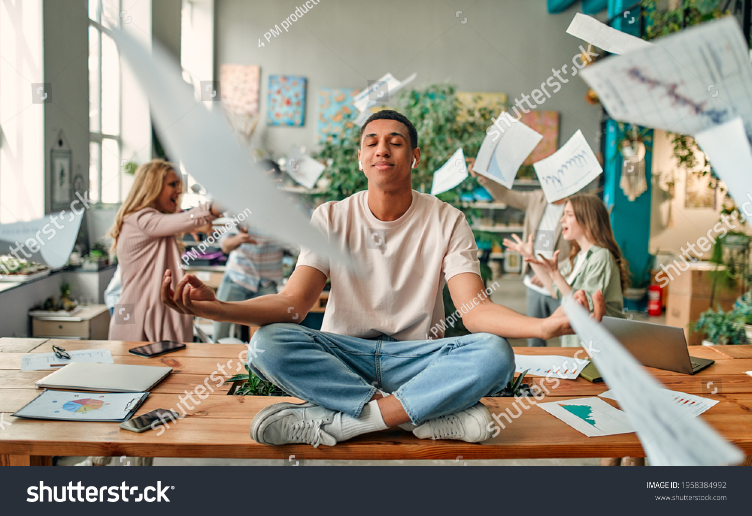 Keep calm and no stress! Young African-American man is sitting in lotus position while his colleagues are arguing nearby. Multiracial people working together in modern office. #1958384992