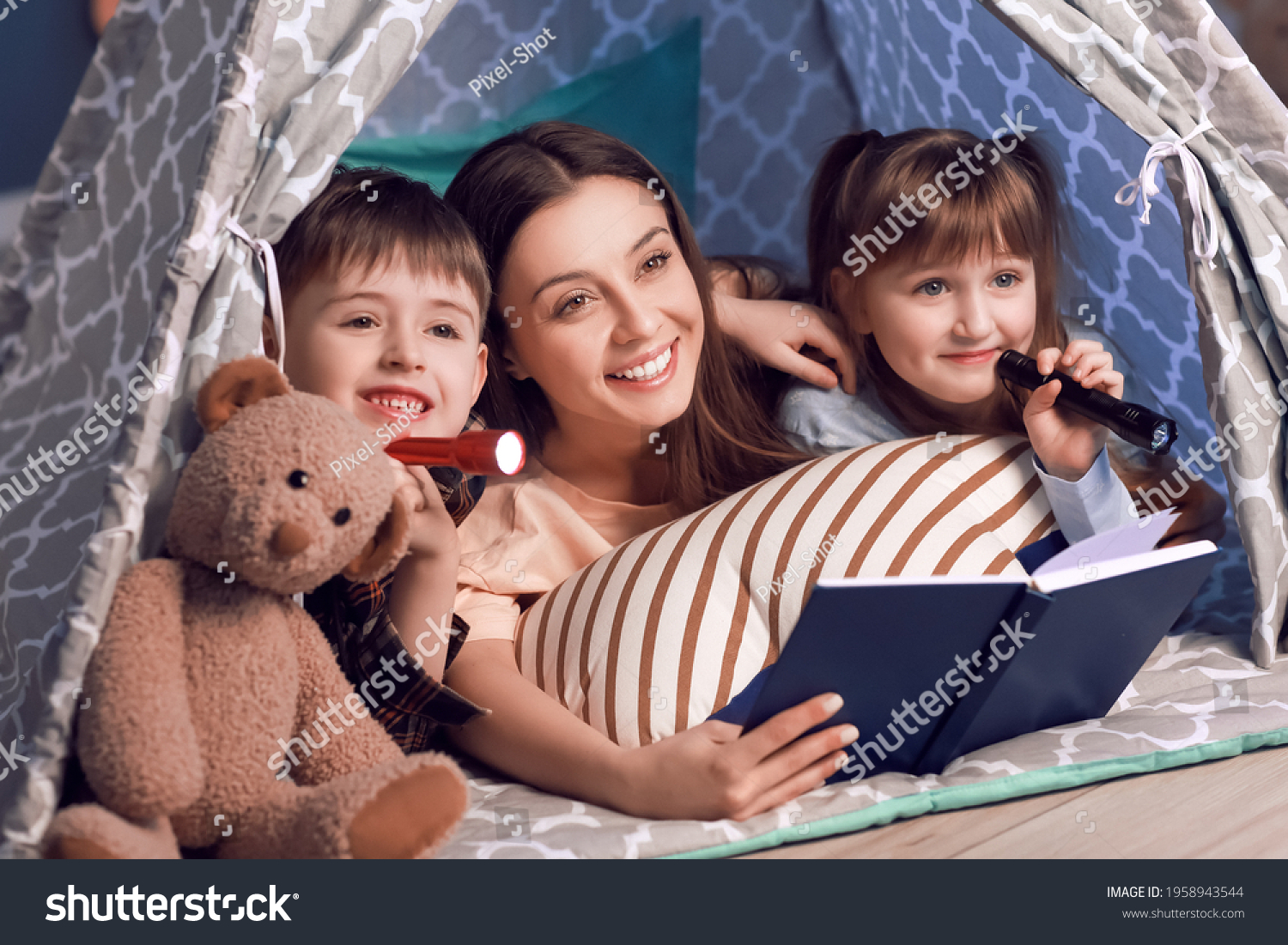 Woman and her little children reading book in play tent at night #1958943544