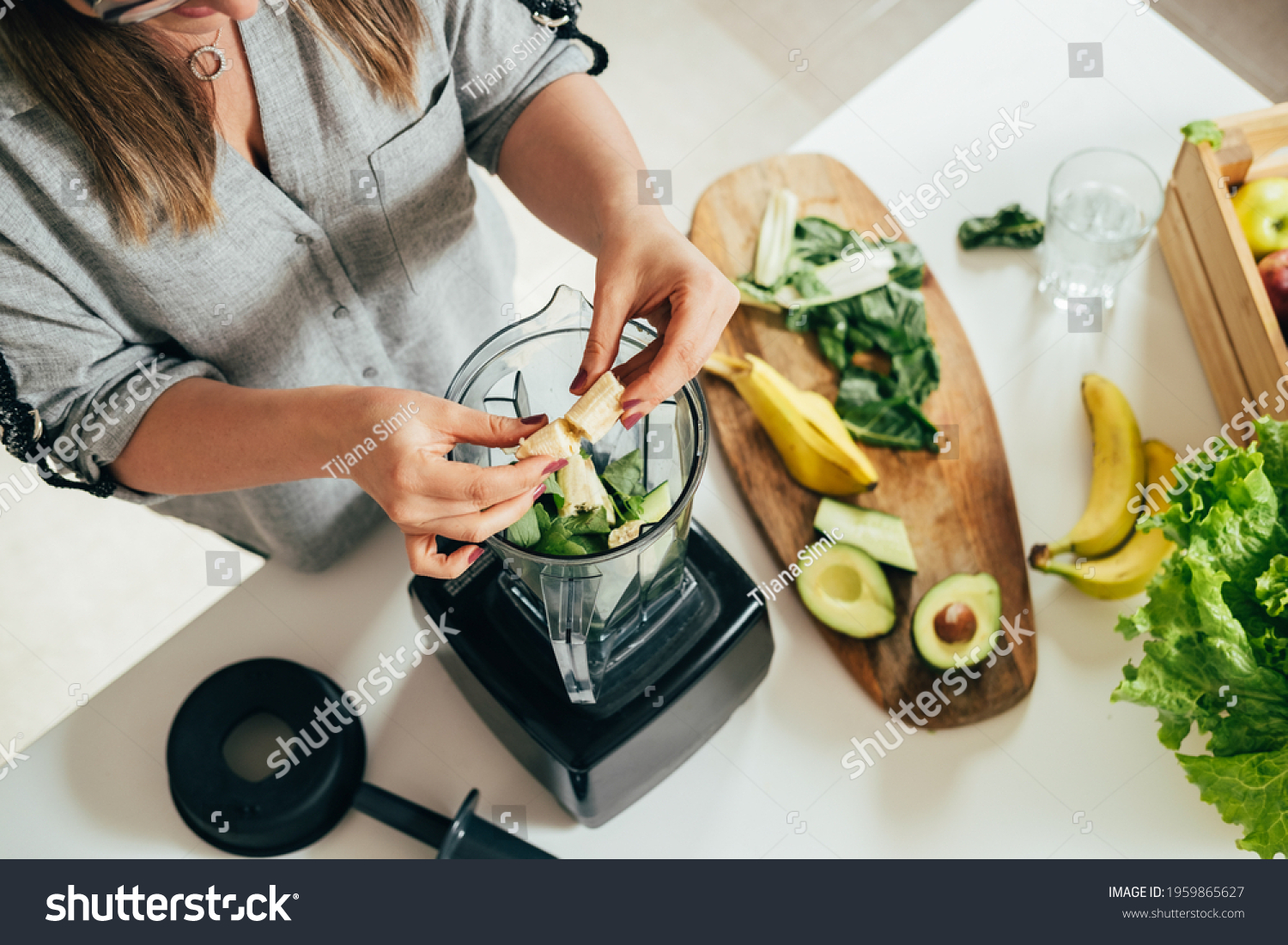 Woman is preparing a healthy detox drink in a blender - a  green smoothie with fresh fruits, green spinach and avocado. Healthy eating concept, ingredients for smoothies on the table, top view #1959865627