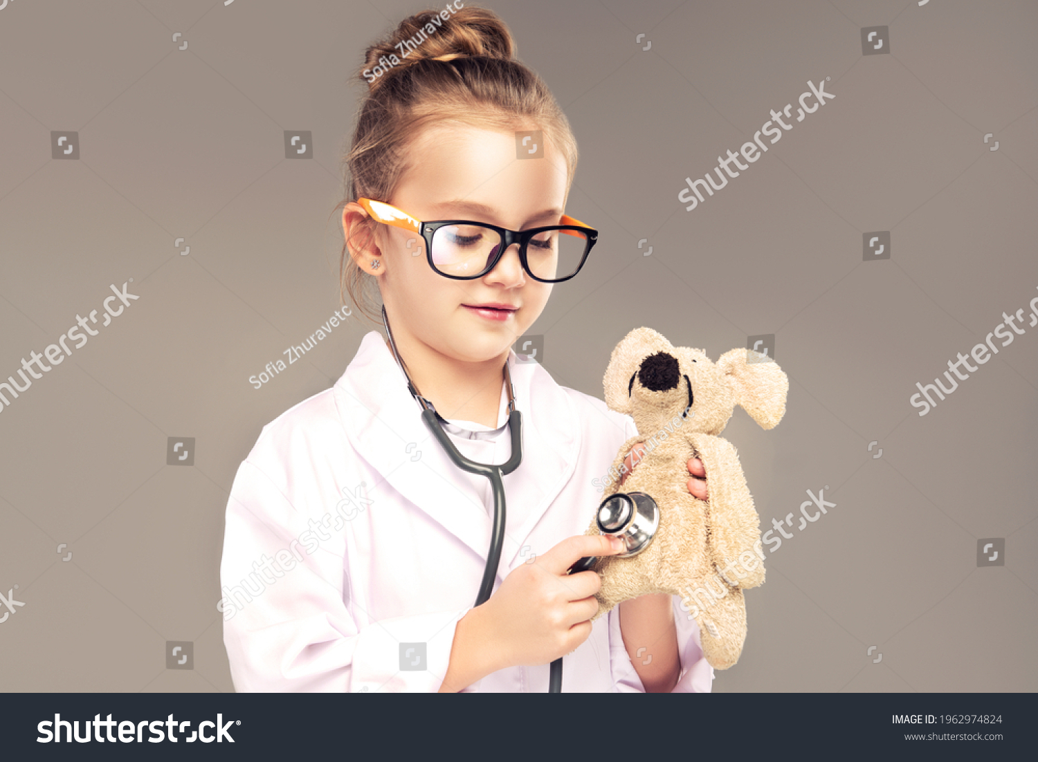 Child girl in a medical gown and stethoscope plays and pretends to be a doctor . Children choose a profession for the future. Happy and smiling baby in the game. Expressive facial emotions #1962974824