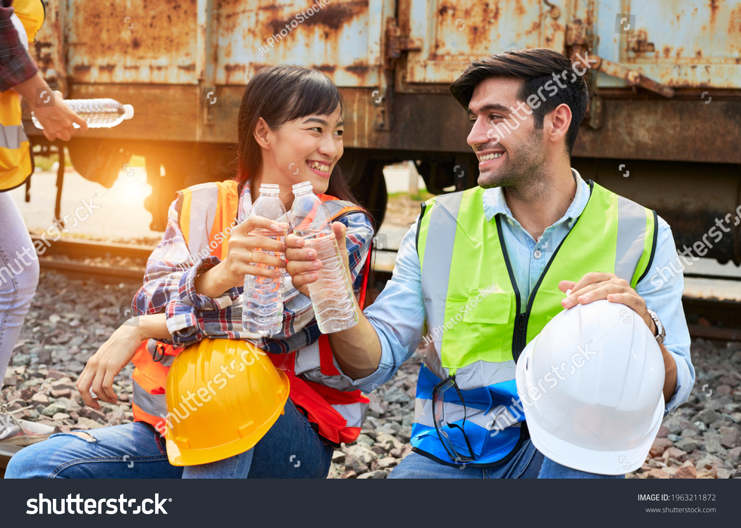 Industrial workers or Rail transport engineers in protective clothing are drinking water to quench their thirst beside the freight train after working hard during the day outdoors. #1963211872