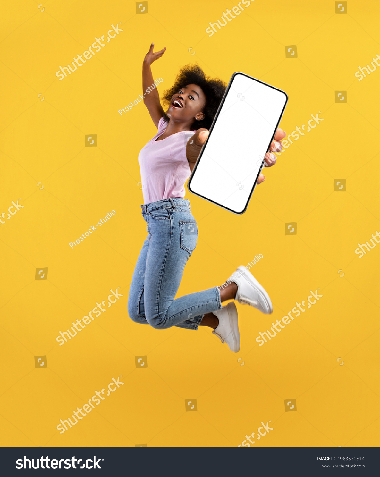 Overjoyed african american young lady showing empty smartphone screen while jumping up over yellow studio background, collage, full size photo. Happy black woman recommending new mobile app #1963530514