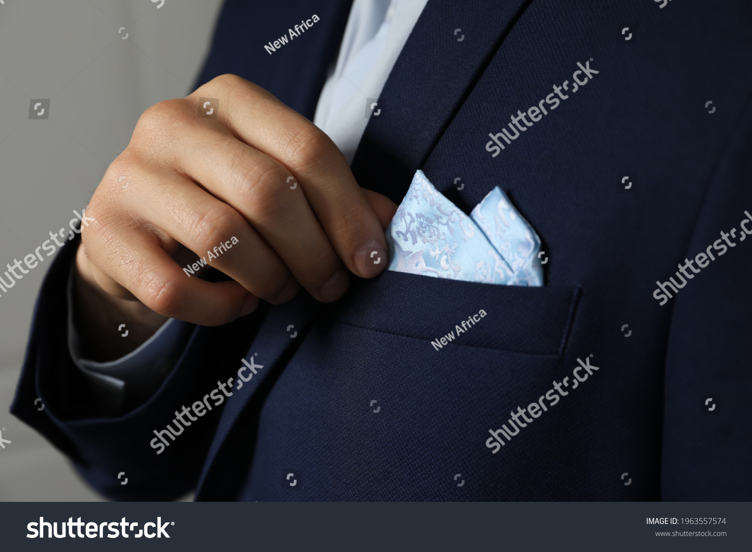 Man fixing handkerchief in breast pocket of his suit on light background, closeup #1963557574