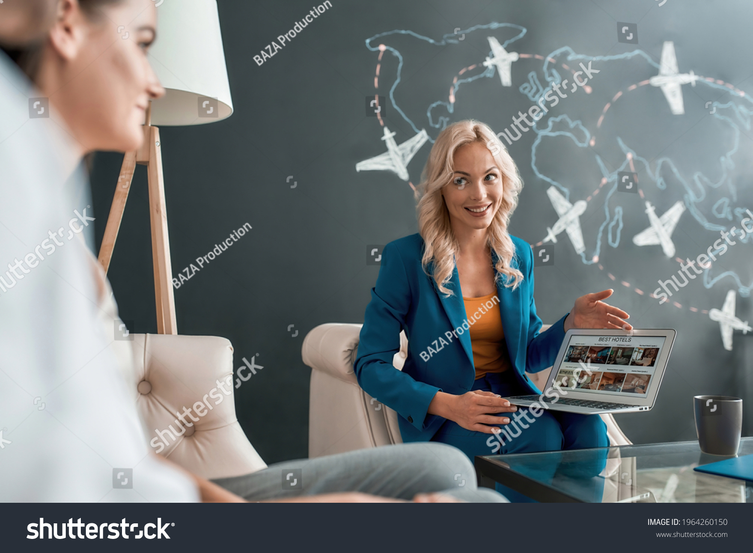 Attractive female travel agent looking at her clients, communicating with them in office and showing tours, using laptop. Tourism, travelling, business concept #1964260150