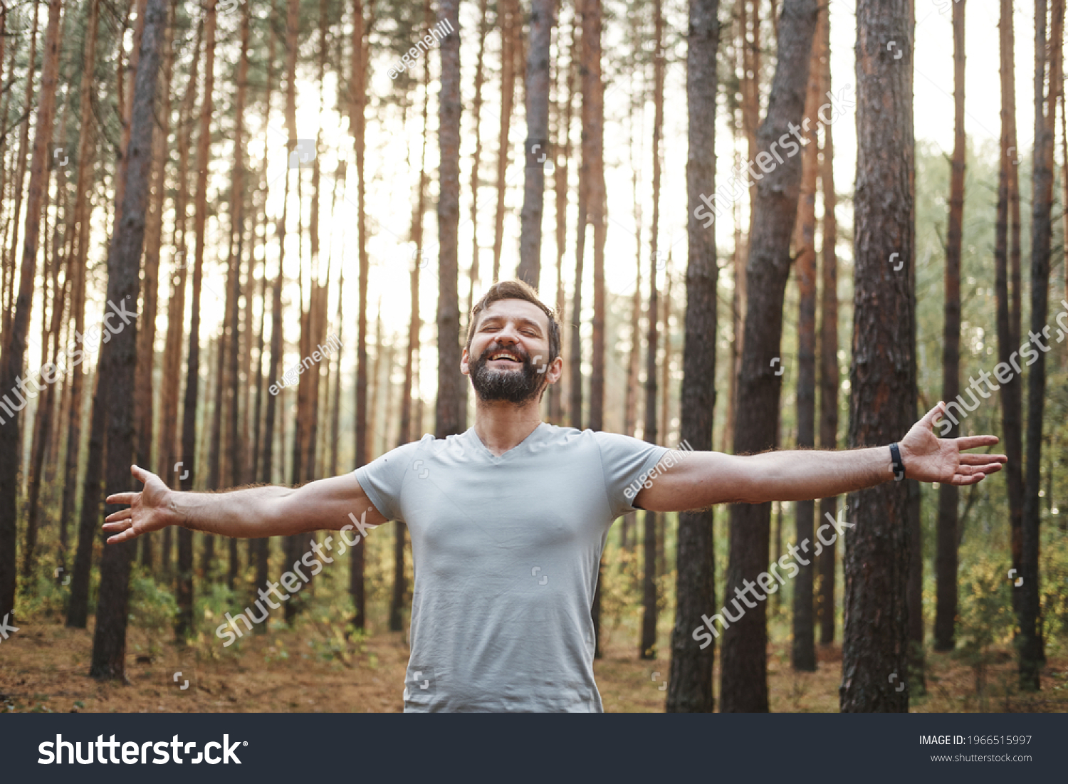 Young happy Caucasian male in the forest. He spread his arms and closed his eyes. Wellness concept and holistic rest #1966515997