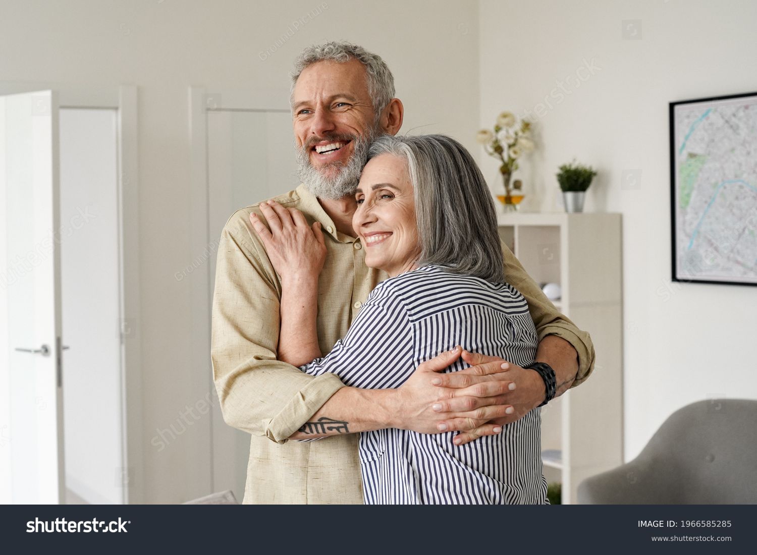 Happy senior adult mature classy couple hugging, bonding, thinking of good future. Carefree cheerful mid age old husband embracing wife looking away dreaming, enjoying wellbeing and love in new house. #1966585285