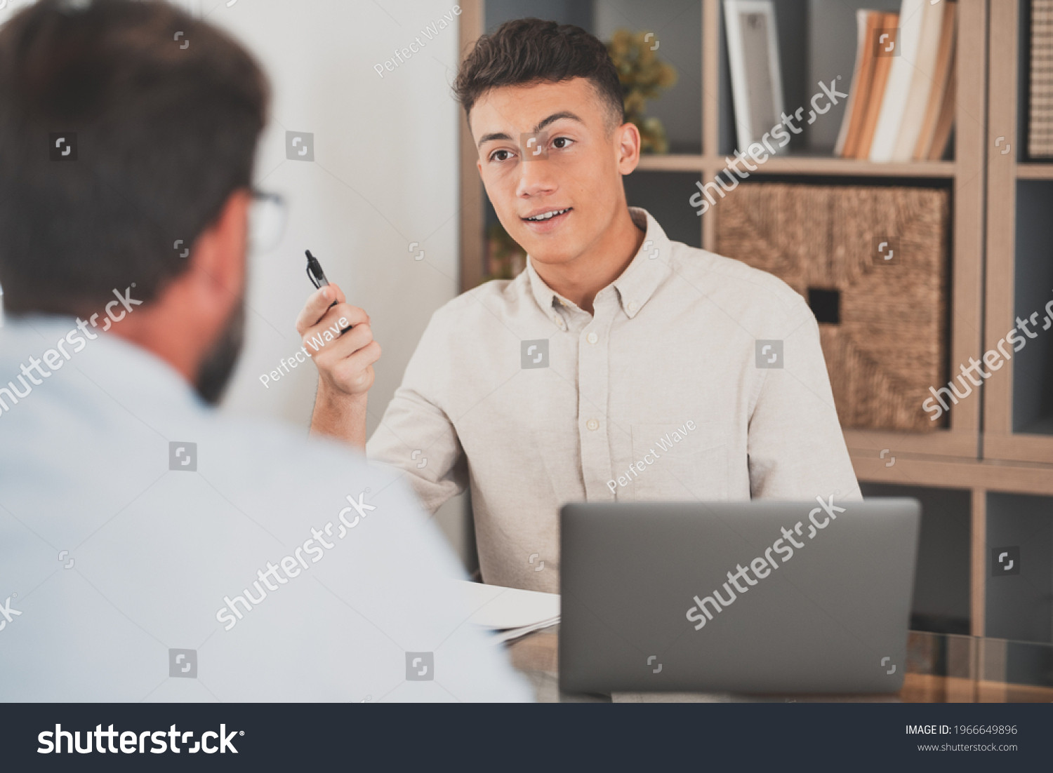 Portrait of teenager man smiling and talking to a man next to her talking about business work together in the office. Businessman working from home indoor. #1966649896