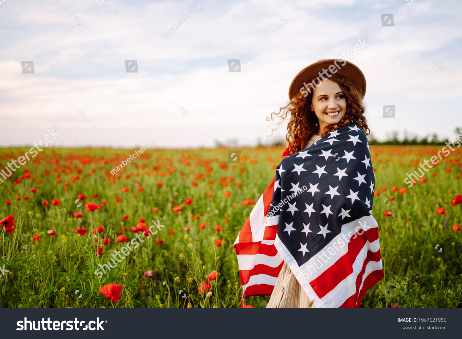 Young woman in hat with the American flag in in the poppy field. Fourth of July. Freedom. Beautiful sunset. Independence Day. Patriotic holiday. #1967621956