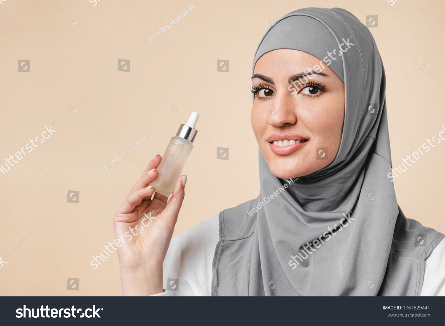 Young pretty arabian muslim islamic woman in hijab using beauty serum for anti-age effect, rejuvenation and pampering. Soft skin, makeup base and cosmetics concept #1967629441