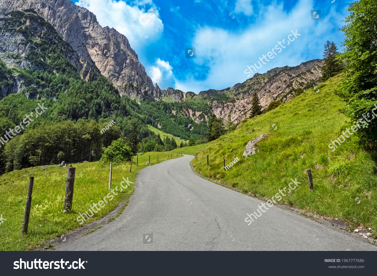 Winding mountain road through green rural alpine landscape with view on Wilder Kaiser, Austrian alps, Austria #1967777686