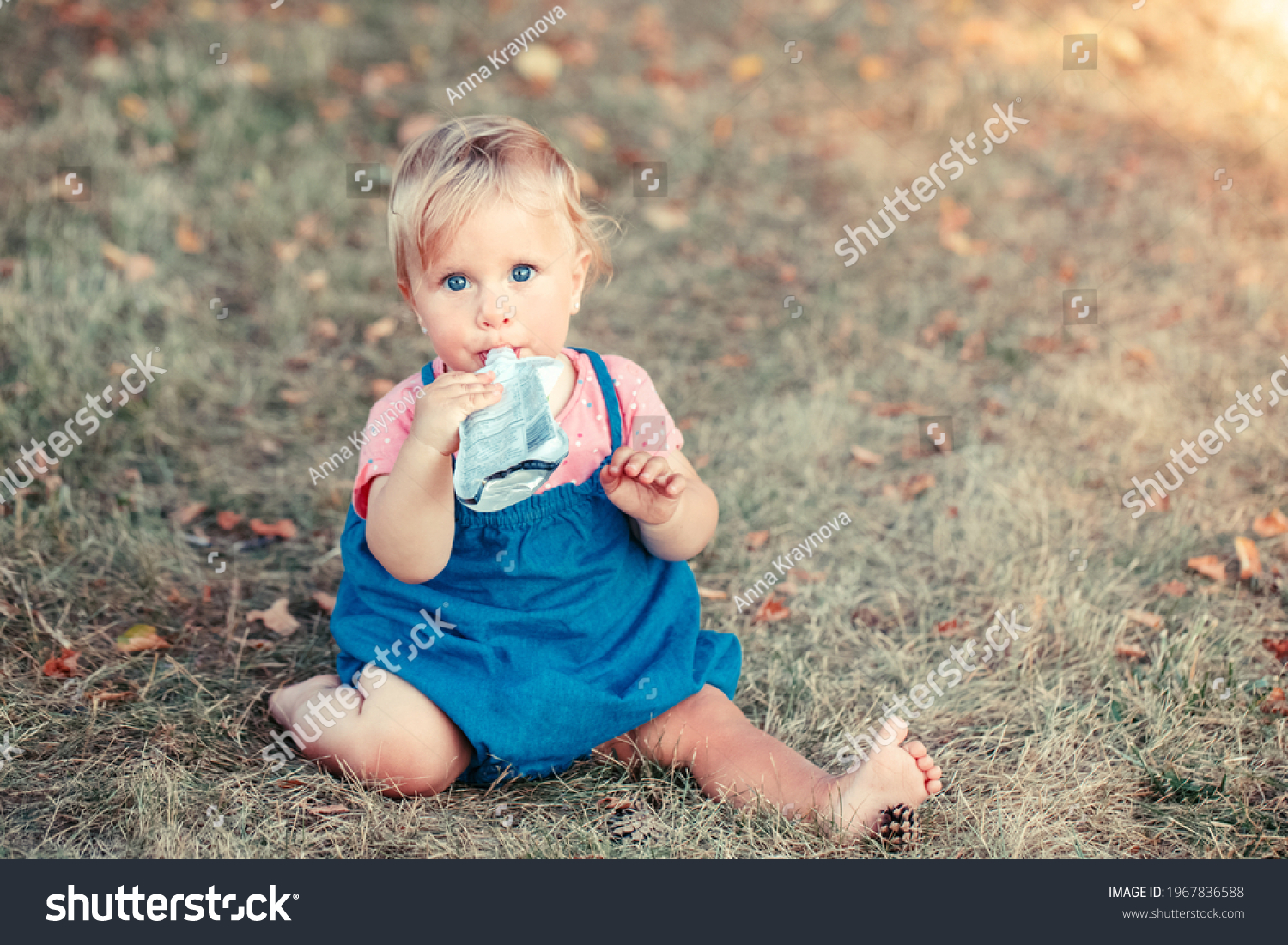 Toddler baby eating baby food organic vegetable fruit puree from pouch. Supplementary solid healthy food meal snack for babies kids. Girl eating outdoor in park on summer day. 
 #1967836588