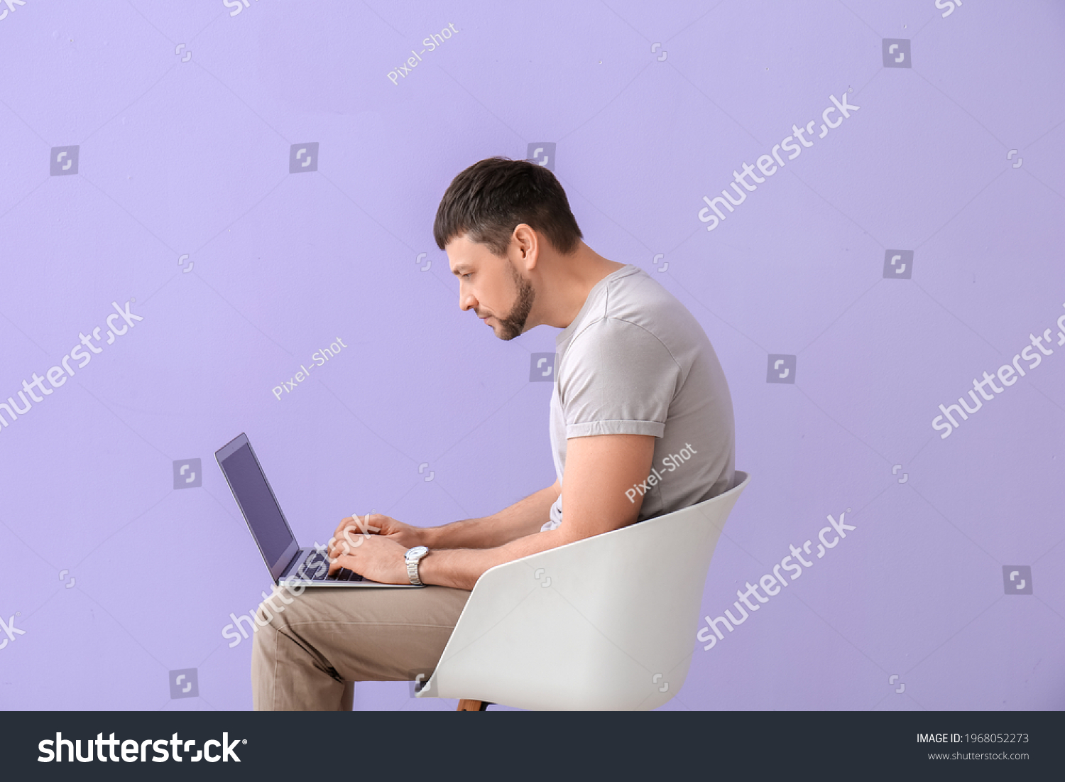 Man with bad posture using laptop while sitting on chair against color background #1968052273