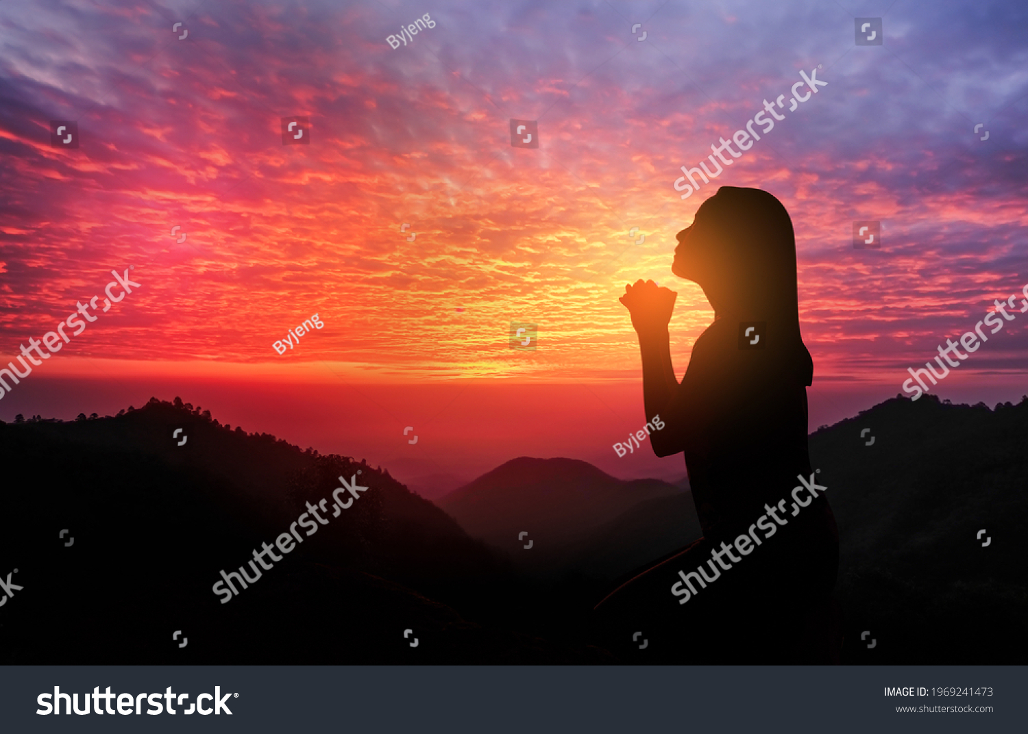 silhouette of women kneeling and praying over beautiful sunset with mountains #1969241473