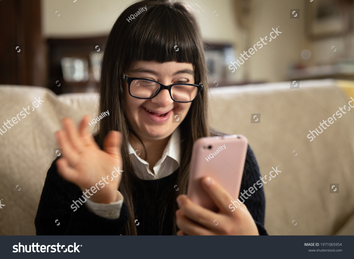 Cinematic shot of happy teen girl with down syndrome making video call with smartphone to friends or family at home. Concept of technology, disability, media, friendship, new generation. #1971065954