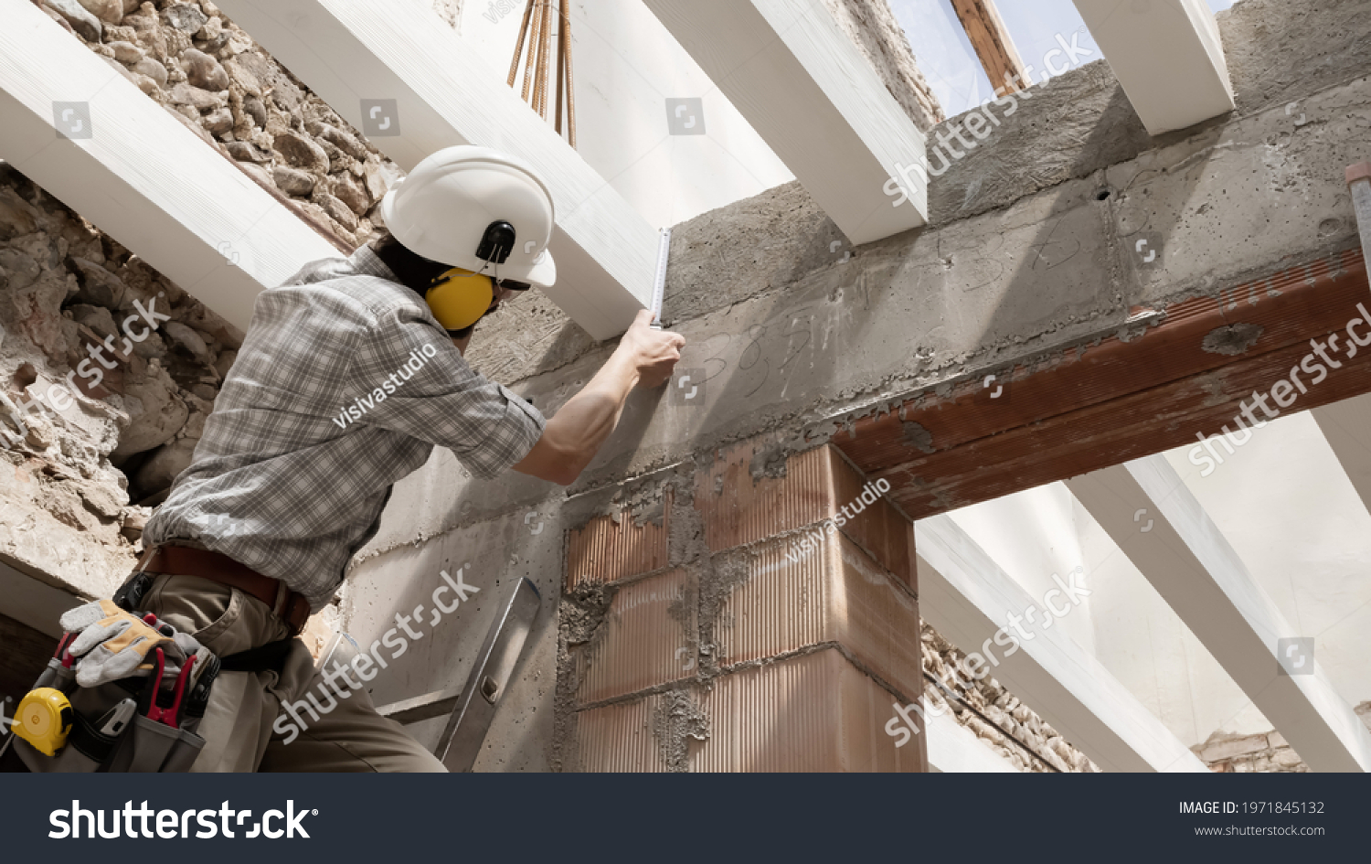 man at work, construction worker wear a helmet, check the measurements and distances of the beams at the base of the foundations of the second floor of house, in renovation building site background #1971845132