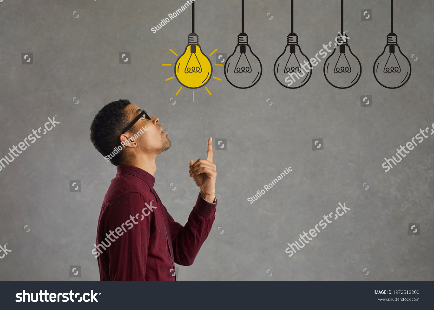 Side profile view young man making choice looking up at several electric light bulbs. Creative Afro American entrepreneur considers different effective business ideas, points finger and picks best one #1972512200