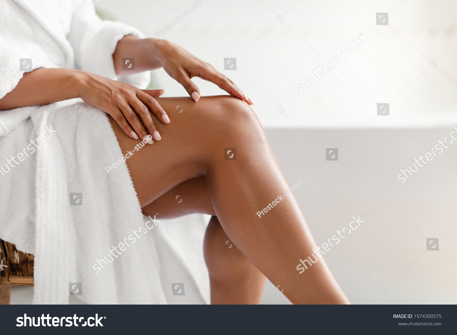 Side View Of Unrecognizable Black Lady Touching Perfect Smooth Legs After Depilation Posing Sitting On Chair In Bathroom At Home. Cropped Shot Of Female Legs. Hair Removal And Body Care #1974300575