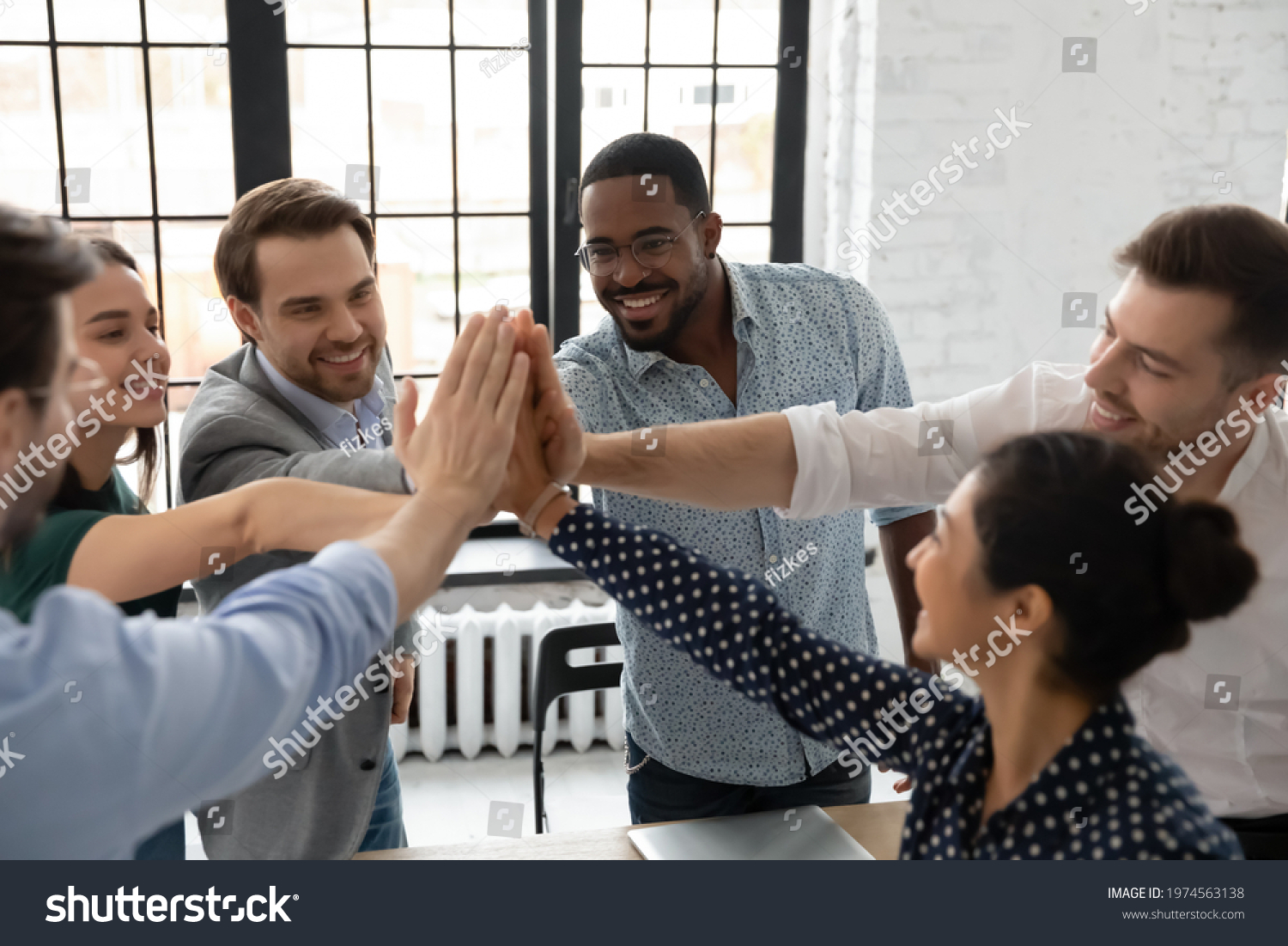 Excited millennial teammates joining hands for giving high fives. Team of happy employees celebrating corporate goal achievement, successful project accomplishment, shared success. Teamwork concept #1974563138