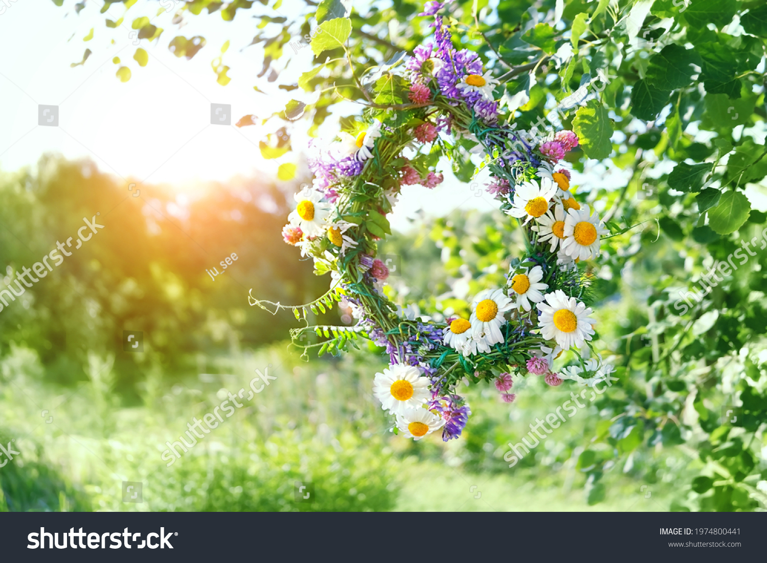 beautiful wreath of meadow flowers hanging on tree, natural sunny green background. floral decor, symbol of Summer Solstice Day, Midsummer. pagan witch traditions, wiccan ritual. Litha sabbat. #1974800441