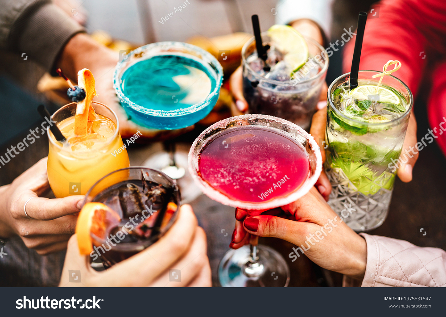 People hands toasting multicolored fancy drinks - Young friends having fun together drinking cocktails at happy hour - Social gathering party time concept on warm vivid filter - Shallow depth of field #1975531547