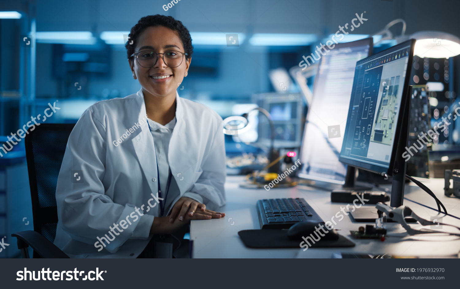 Beautiful Black Latin Woman Wearing Glasses Smiling Charmingly Looking at Camera. Young Intelligent Female Scientist Working in Laboratory. Technological Laboratory in Bokeh Blue as Background #1976932970