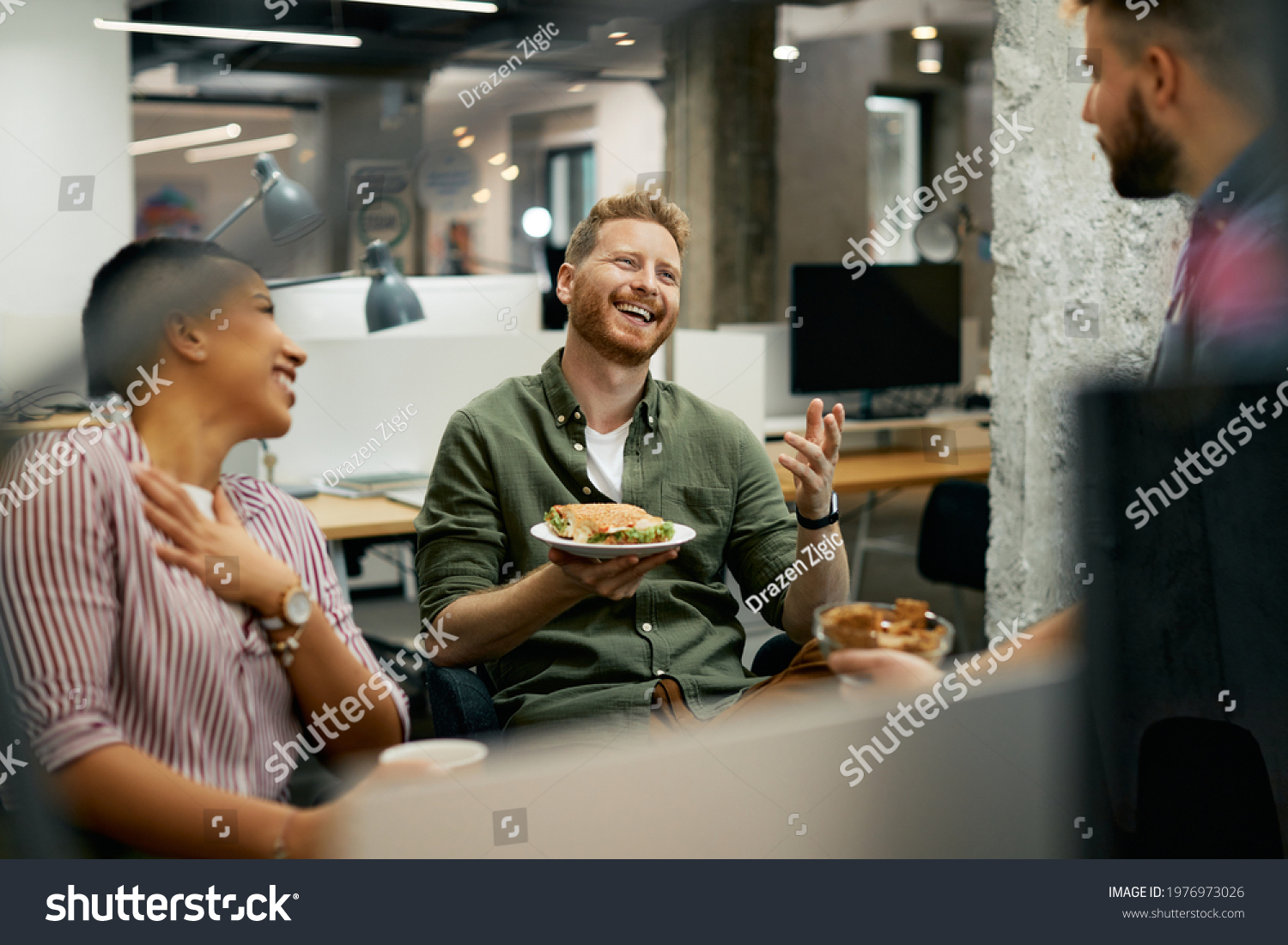 Team of happy freelancers having fun while communicating on lunch break in the office. Focus is on redhead man.  #1976973026