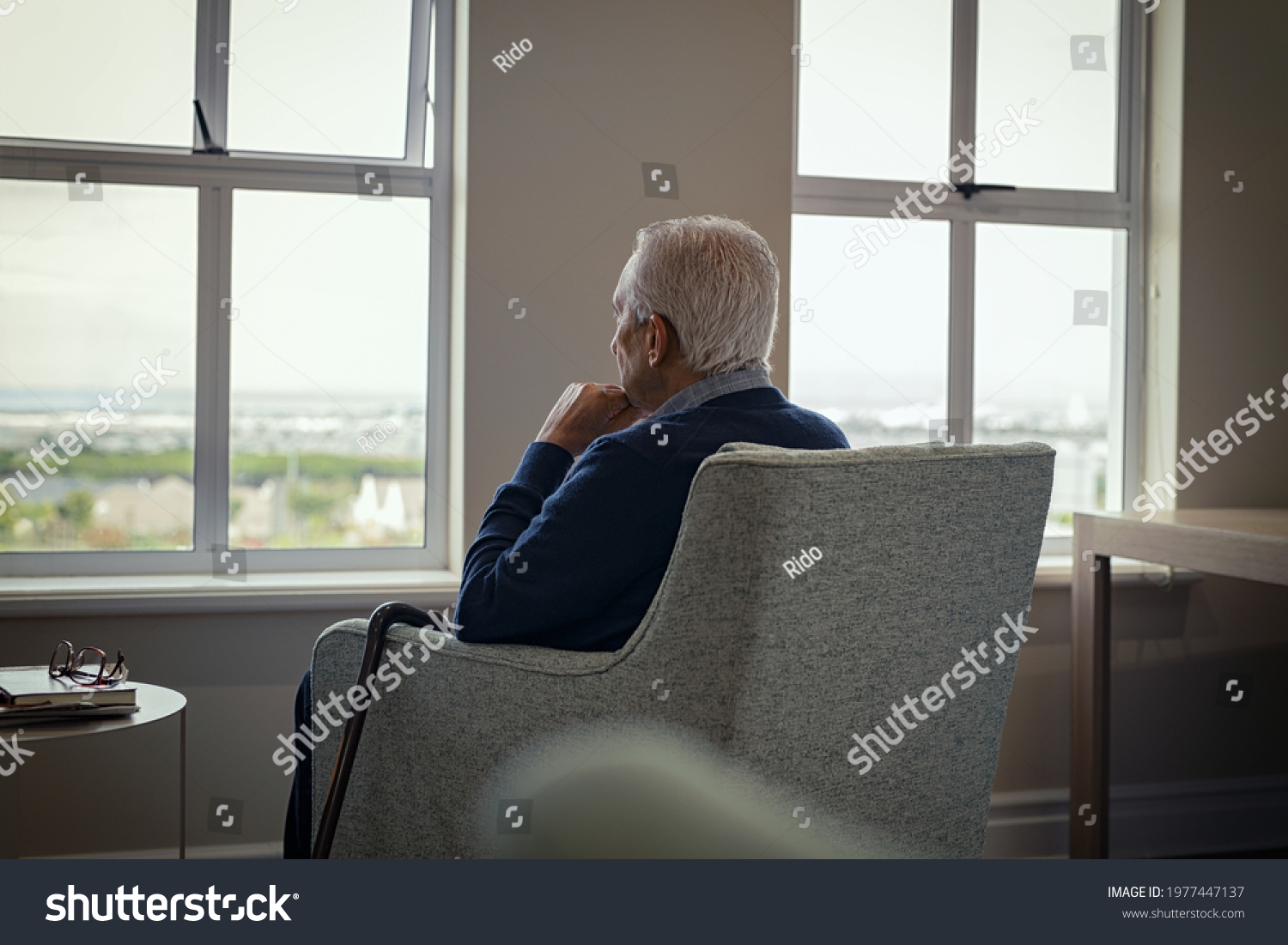 Rear view of senior man sitting on armchair and looking through the window. Lonely old man sitting at home near window during covid19 outbreak. Thoughtful retired man abandoned at nursing home. #1977447137