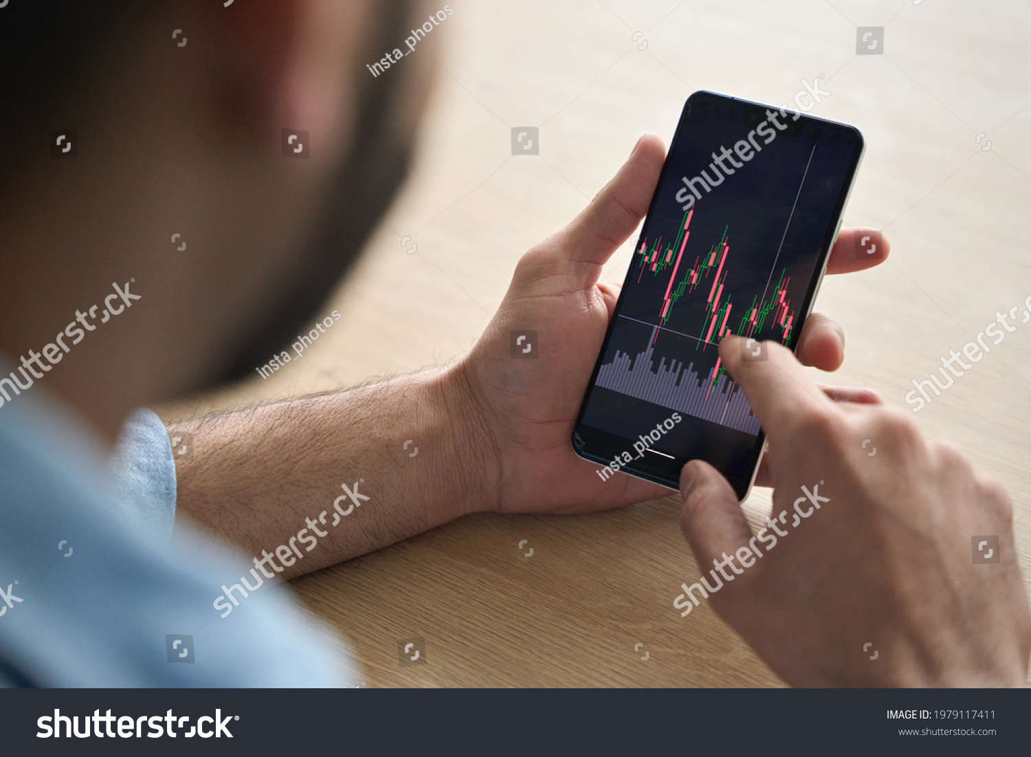 Over shoulder close up view of male analyst broker's hands holding touch screen device smartphone using tech ecommerce application of finance stock markets with graphs and numbers. #1979117411