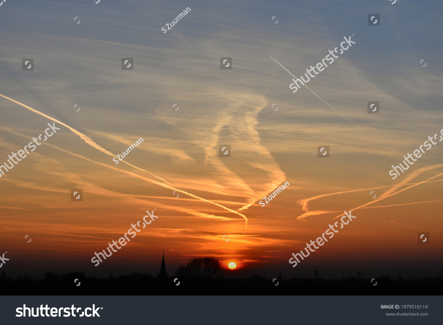 contrails in the sky at sunset due to engine exhaust produced by airplanes #1979516114