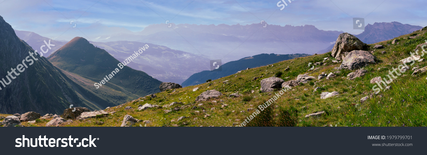 Panorama of the Alpine mountains. Ridges and peaks are visible in the background. Large and small stones lie on the grassy slope. #1979799701