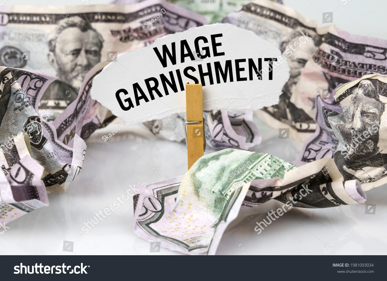 Business and finance concept. There are dollars on the table and there is a clothespin with paper on which it is written - WAGE GARNISHMENT #1981093034