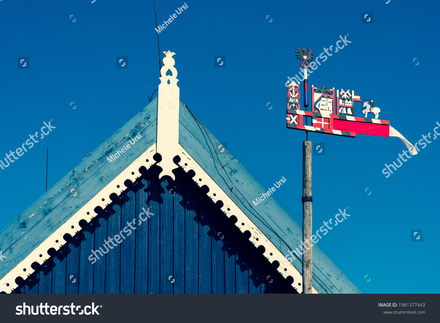Beautiful colorful weathercock waving in the Curonian Spit in Nida fishermen's village, Lithuania, Europe with blue sky and roof of a wooden house #1981377443