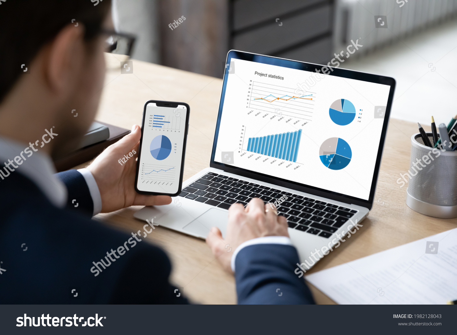 Business marketer using professional app for marketing data analyzing on laptop and smartphone screens, studying financial graphs, comparing diagrams on phone and computer. Analysis concept #1982128043