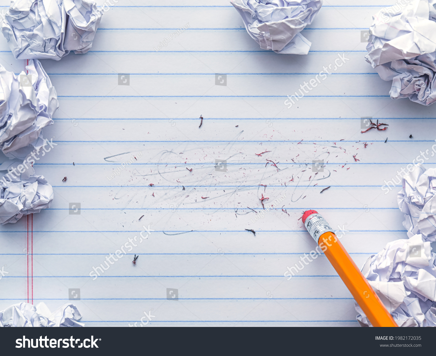 School supplies of blank lined notebook paper with eraser marks and erased pencil writing, surrounded by balled up paper and a pencil eraser. Studying or writing mistakes concept. #1982172035