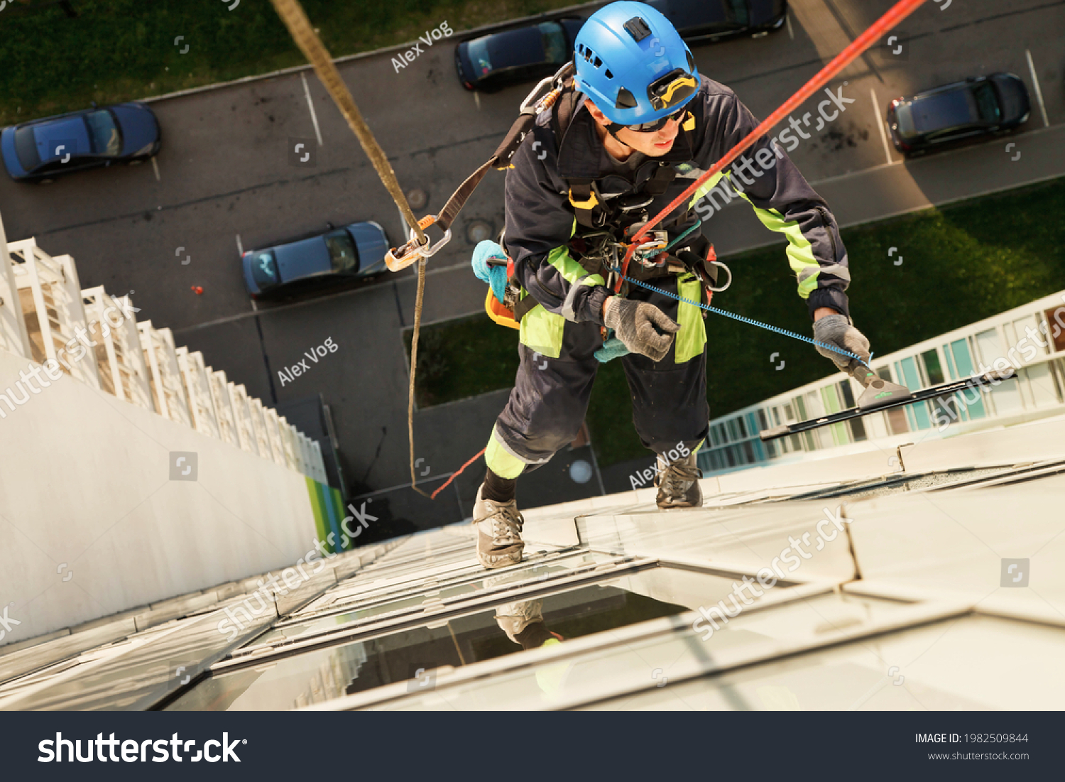 Industrial mountaineering worker hangs over residential facade building while washing exterior facade glazing. Rope access laborer hangs on wall of house. Concept of urban works. Copy space for site #1982509844